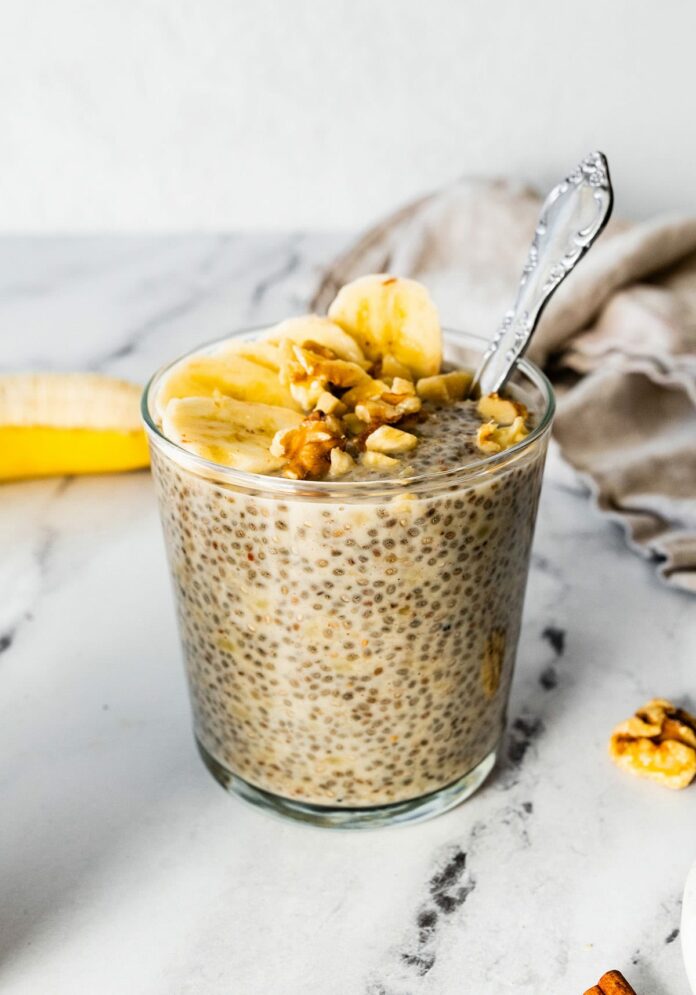 Banana chia pudding in a glass cup, topped with banana slices and walnuts.