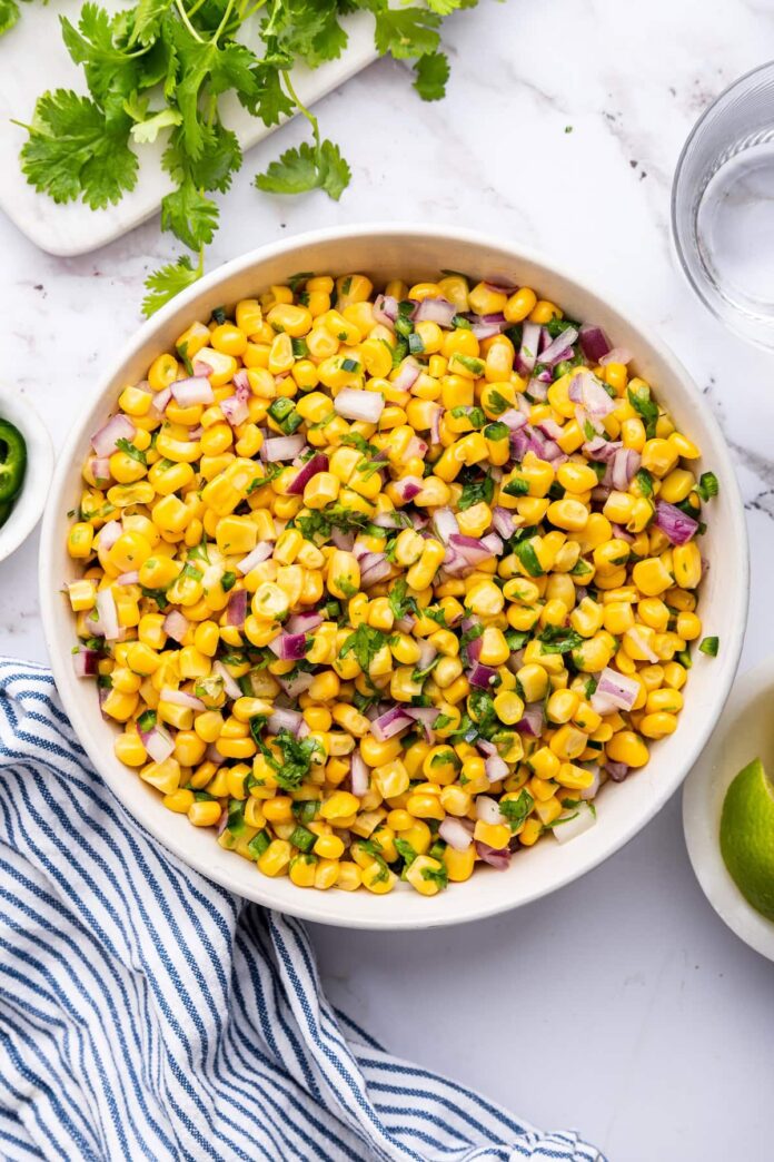 Corn mixed with red onion, cilantro and jalapeño in a white serving bowl.
