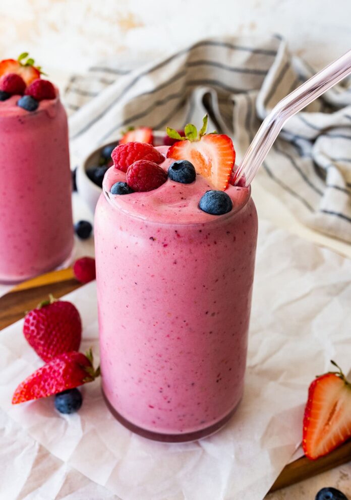 Two glasses filled with the berry kefir smoothie topped with fresh blueberries, raspberries and strawberries.