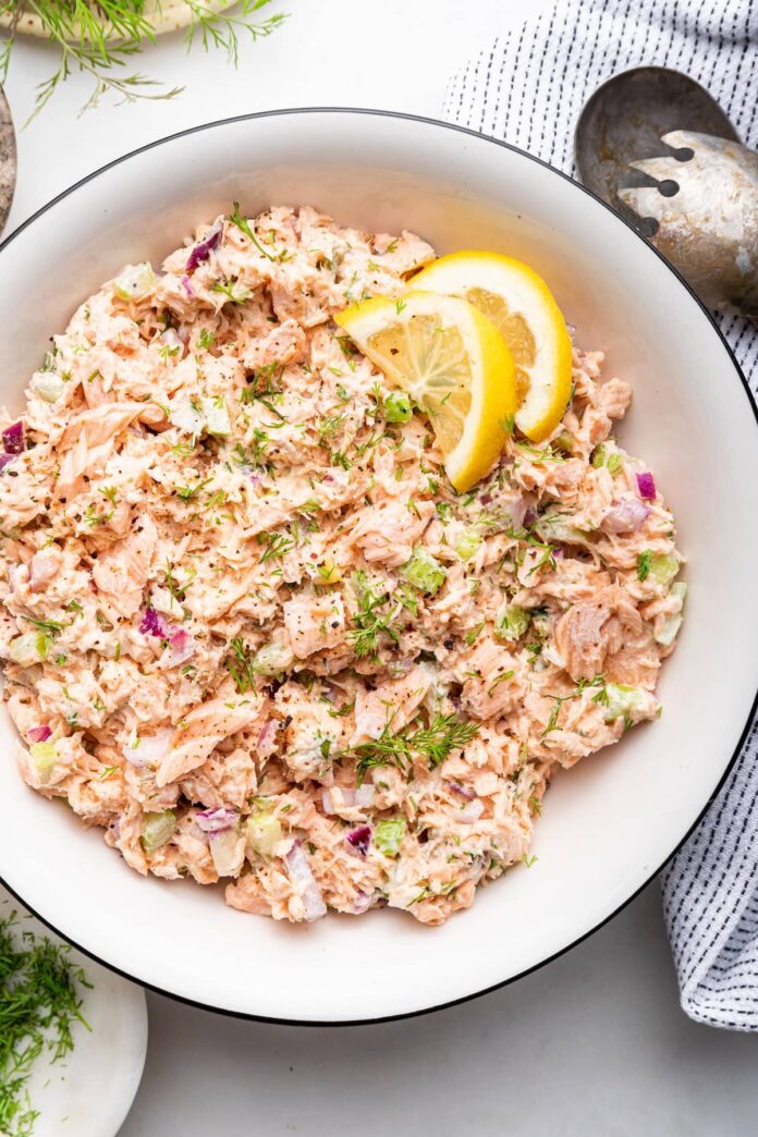 Salmon salad in a white bowl with two lemon slices.