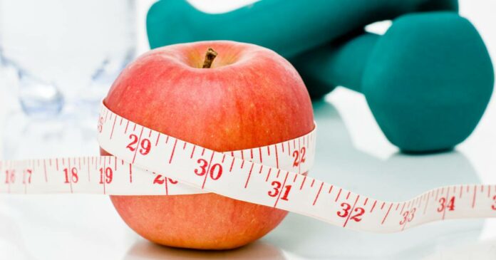 Measuring tape wrapped around a red apple with weights in the background