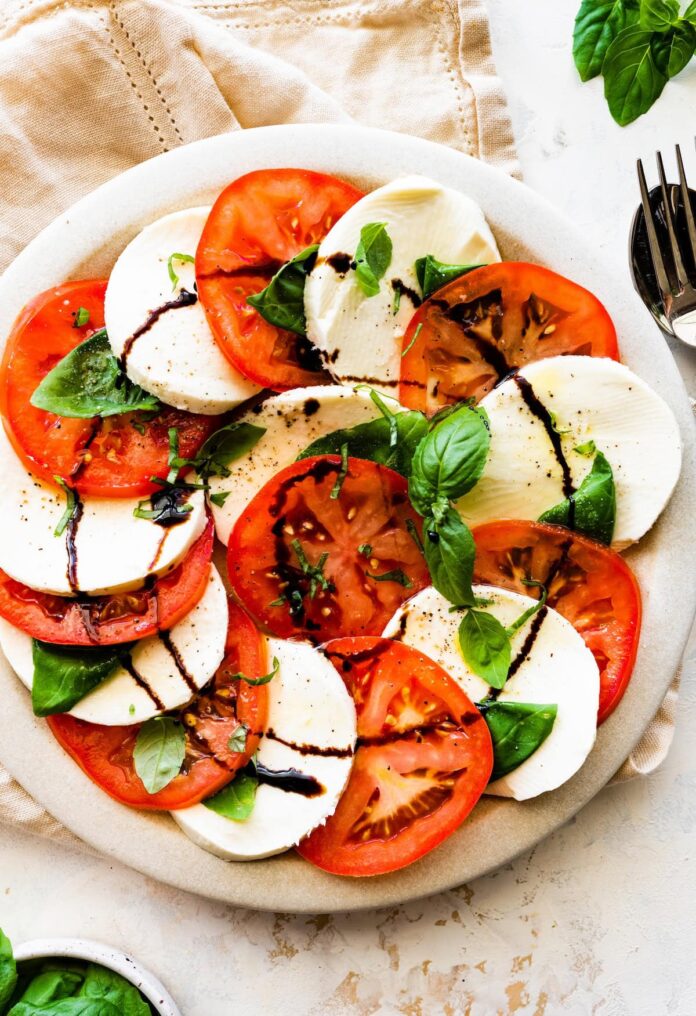 A caprese salad on a plate with sliced mozzarella cheese, sliced tomatoes, fresh basil, and a drizzle of balsamic vinegar.
