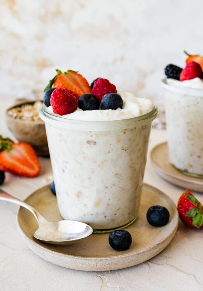 Overnight oats with yogurt in a glass cup, on a small plate, and topped with fresh berries.