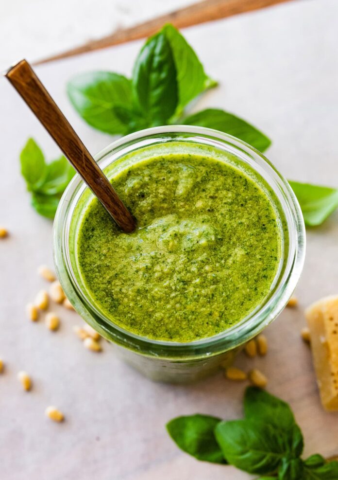 Overhead photo of a glass jar full of homemade pesto with a spoon in the jar.