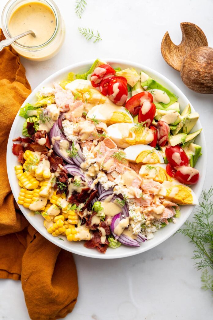 A salmon cobb salad in a bowl with fresh vegetables and a drizzle of a creamy honey mustard dressing.