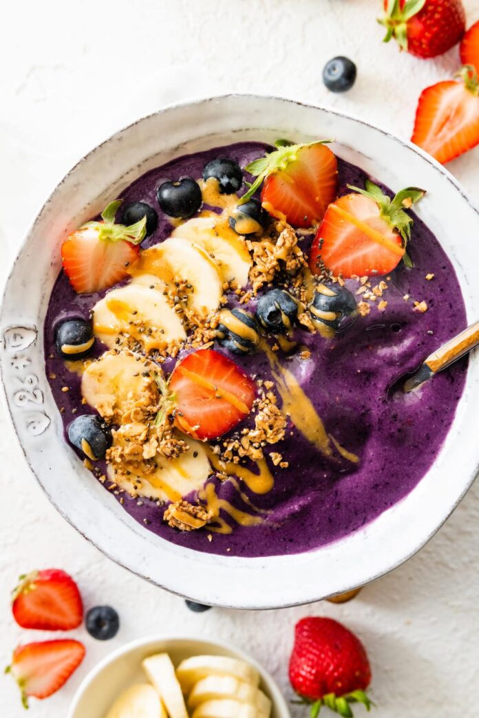 A smoothie bowl topped with fresh fruit, granola, and a drizzle of almond butter.