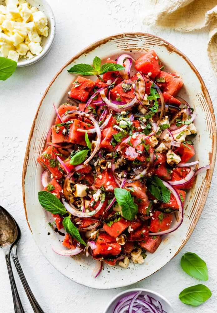 A watermelon salad with crumbled feta cheese, fresh basil, balsamic vinegar, and red onions.