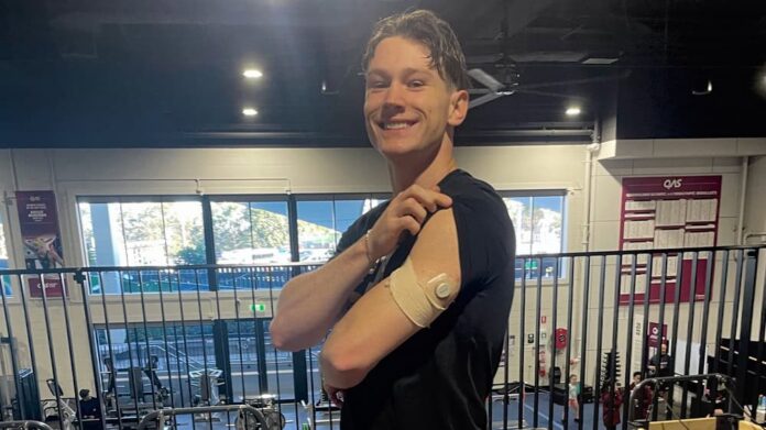 Lachie Kennedy shows his left arm with CGM sensor while lifting his black tshirt sleeve.